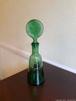 Full view of green glass decanter with face stopper on tabletop