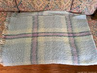Full view of the folded blanket showing pastel plaid pattern and fringe edges on sofa