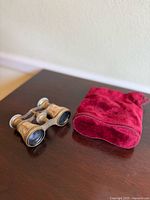 Photo showing the opera glasses next to the red velvet pouch on a wood surface.