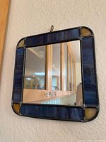 Full view of square mirror on wall showing blue stained glass border and amber corner accents
