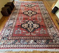 Full view of coral rose colored Caucasian pattern area rug on hardwood floor