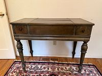 Front view of closed wooden spinet desk showing drawers and turned legs