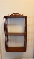 Front view of vintage wooden wall display shelf showing two tiers and decorative top arch.
