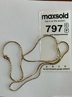 Gold chain necklace coiled beside lot tag