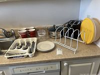 Countertop view showing toaster, pots, mugs, cutlery tray, plates, rack, yellow lid