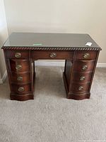 Front view of desk showing seven drawers, brass pulls, glass top