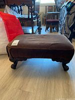 Front angled view showing brown cushioned top and carved wood legs