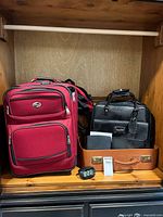 Overview of all items in cabinet: red suitcase, black briefcase, brown attache case, portable DVD player, alarm clock