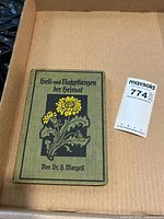 Front cover of olive-green cloth book with yellow flower illustration and lot tag visible