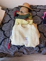 Folded cream sweater with tag, yellow and green sweaters underneath, two straw hats stacked, red-handle umbrella