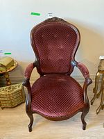 Front view of Victorian parlor chair showing carved crest, button tufting, burgundy velvet upholstery