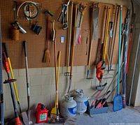 Wide view of pegboard with long-handled tools, saws, brooms, string trimmer, propane tanks and caddy