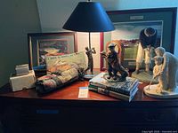 Overall lot on dresser showing lamp, figurines, books, pillow, framed prints