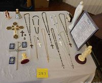Overall lot layout on table showing rosaries, crosses, figurines, framed print, medals, cases