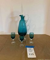 Full view of teal decanter with stopper and three cordial glasses