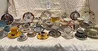 Full lot overview showing two rows of assorted teacups, saucers and small plates on table