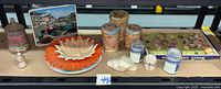 Full lot on shelf showing tins, plates, shells, sand art kit and sand bottles