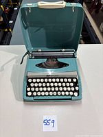 Top view of teal Smith-Corona Corsair Deluxe typewriter with lid open and handle visible