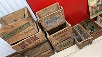 Stacked vintage crates showing Canada Dry, Kik Cola, Pepsi-Cola, Fanta, Reinhart, 7-Up and additional bottle crate