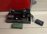 Full view of Singer sewing machine on base with foot pedal and green attachment box