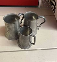 Three pewter tankards standing upright showing exterior engraving and handle styles