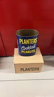 Blue metal Planters Cocktail Peanuts can on top of carton