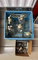 Five seltzer bottles in blue crate, plus box of parts visible