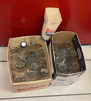 Two boxes containing multiple clear glass milk bottles and one paperboard milk carton