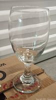 Single clear stemmed drinking glass on cardboard surface showing shape and clarity