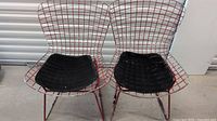 Two red wire frame Mid-Century Modern chairs with black seat cushions side by side in storage area.