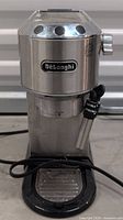 Front view of stainless steel Delonghi espresso machine with steam wand and control buttons visible.
