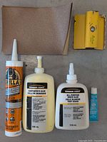 Overview of glue bottles, sandpaper sheets, and scraper tool on concrete floor.