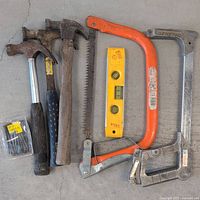 Photo showing 3 hammers, orange handsaw, spirit level, and 2 metal frame saws on concrete floor