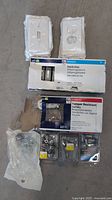 Overview of lot showing Leviton switches in original packaging, Tradeport tamper resistant outlet box, several white switch and outlet wall plates, and assorted packaged hardware.