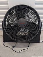 Front view of the Honeywell black box fan showing the three black blades behind a round grille and the Honeywell logo at the center.