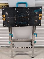 Wolfcraft Master 750 Ergo machine table folded with black top showing grid and yellow clamps, blue handle visible.