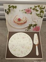 Top view of the cake plate and cake server inside original box with floral design on lid.