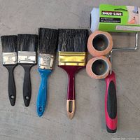 Paint brushes and roller with sleeves laid out on floor, showing various sizes and handle colors