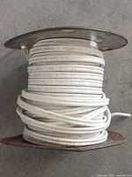 Side view of rusted metal spool with white Romex wire wound around it