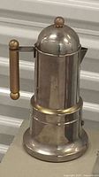 Front angle of stainless steel stove top espresso maker showing brass handle and dome lid.