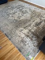 Full view of the large grey area rug laid out on a wood floor showing its pattern and condition.