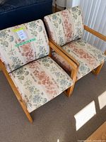 Two matching oak frame chairs with floral upholstery, arranged side by side on a carpeted floor.