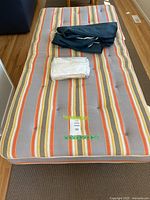 Fold away cot bed with mattress covered in striped fabric and folded bedding on top