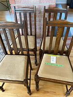 Four vintage oak dining chairs showing the front view, barley twist legs, vertical slat backs, and beige upholstered seats.