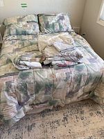 Double bed made with bedding and blanket in patchwork colors of green, beige, and pink, mattress covered with bed bug protector not visible.