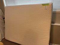 Foam mattress standing vertically showing front side with tag and measuring tape on corner.