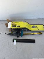 Yardworks electric hedge trimmer displayed alongside its yellow and black original box showing specifications and features.