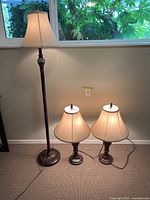 Full view of one floor lamp and two table lamps placed on carpet with a window background.