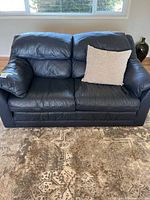 Front view of navy blue leather two-seater sofa with one light beige throw cushion