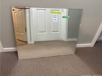 Full view of the rectangular beveled mirror placed on carpet floor, reflecting part of a door and wall.